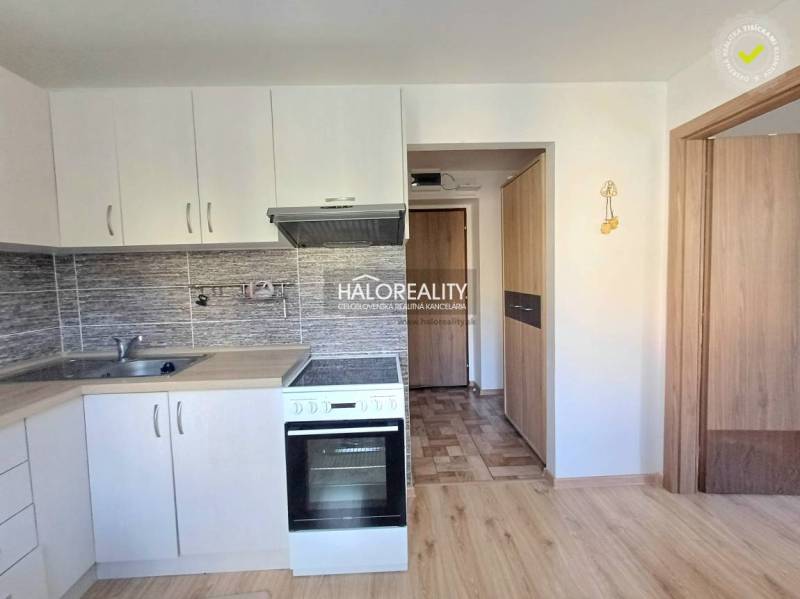 A kitchen unit with white cabinets and a wooden decor floor in a studio apartment.