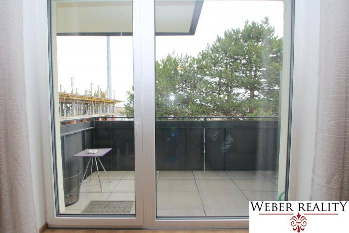 A balcony with sliding doors and a view of trees in a studio apartment on Broskyňová Street in Rovinka.