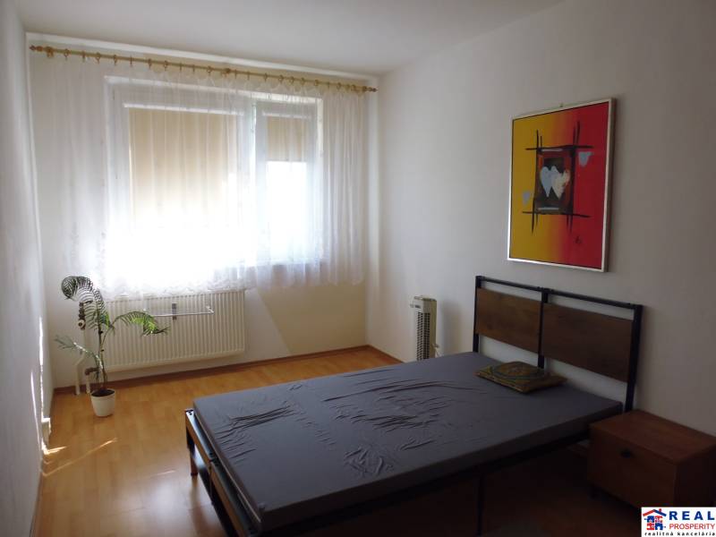 A stylish bedroom in a two-room apartment with a wooden decor floor and an artistic painting.