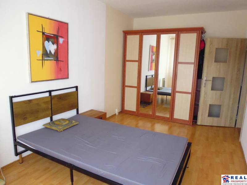 Bedroom with a bed, wooden decor flooring, and a wardrobe in a 2-room apartment.