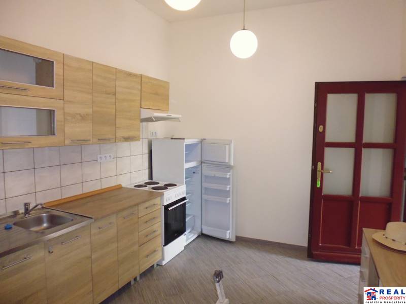 A kitchen with wooden cabinets, a wooden-patterned floor, and white appliances in a 3-room apartment.