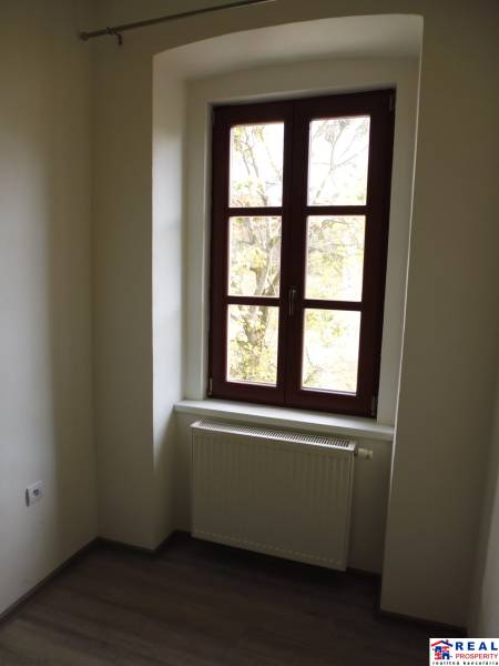 A room with a large window, a radiator, and a floor with a wooden decor in a 3-room apartment.