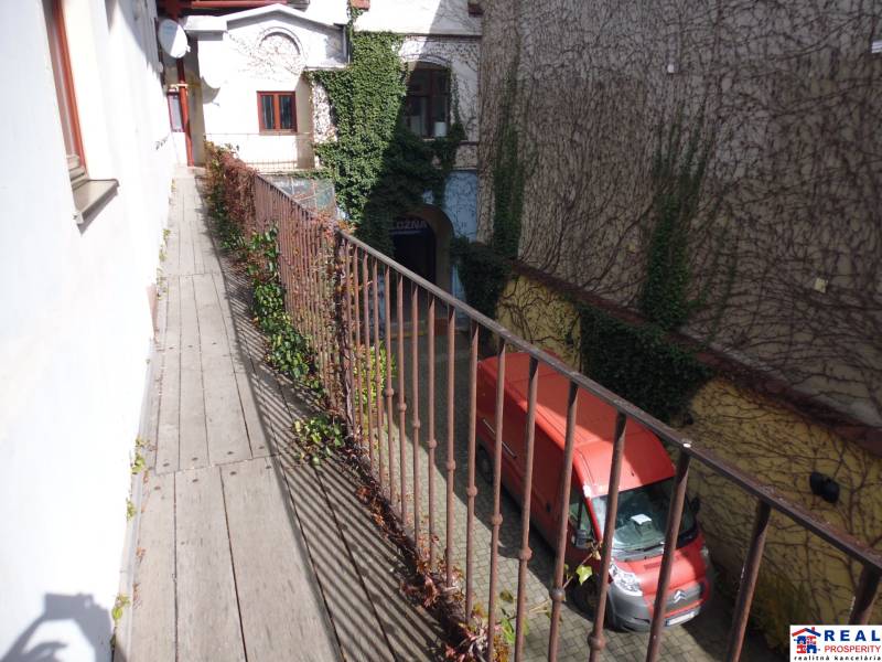 Narrow balcony with wooden decor above the courtyard and a red van, Main Street, Prešov.