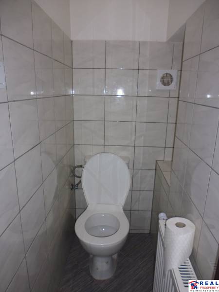 A toilet in a 3-room apartment with tiles and a ventilation opening.