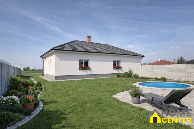 A family house in Zemianska Olča with a lawn, a swimming pool, and flower plantings on the property.