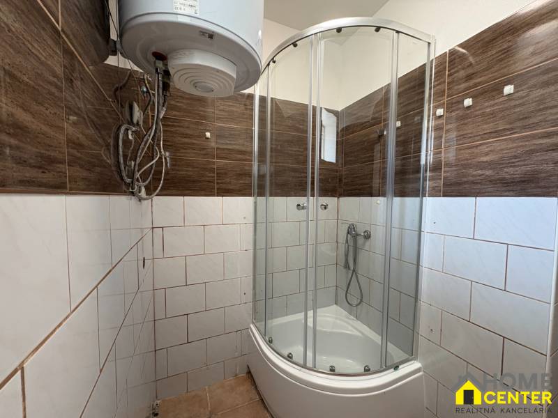 A bathroom in a family house with a corner shower, electric boiler, and brown tiles.