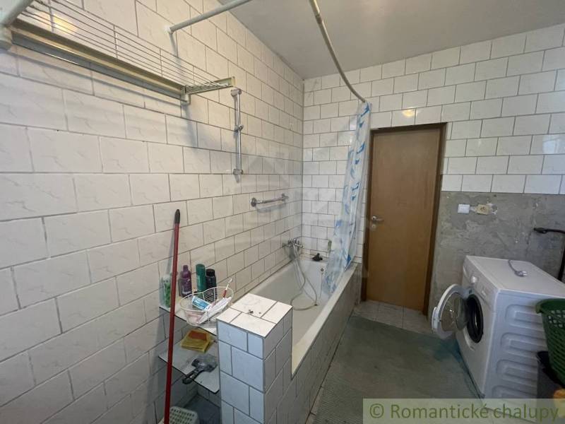 A bathroom in a family house with a bathtub, a washing machine, and tiled walls.