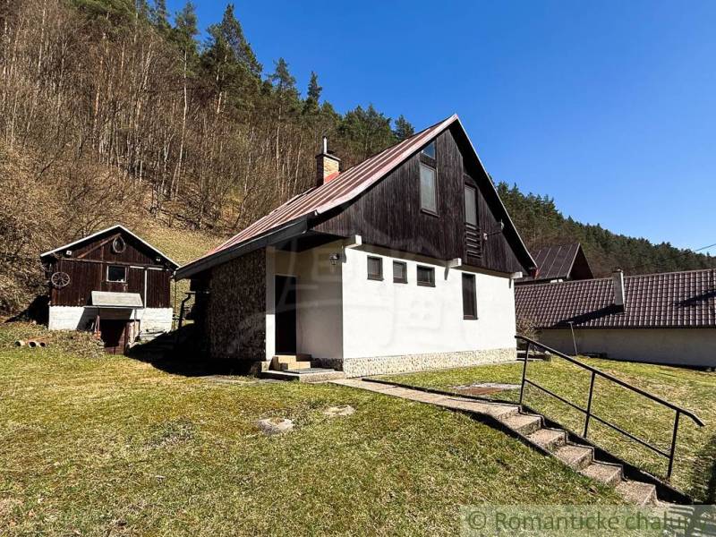 A cottage in Moštenica, surrounded by nature and forest, with a clear sky and grassy land.