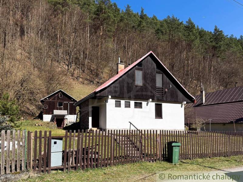 A cottage in Moštenica surrounded by forests, a fence and a trash can in the yard.