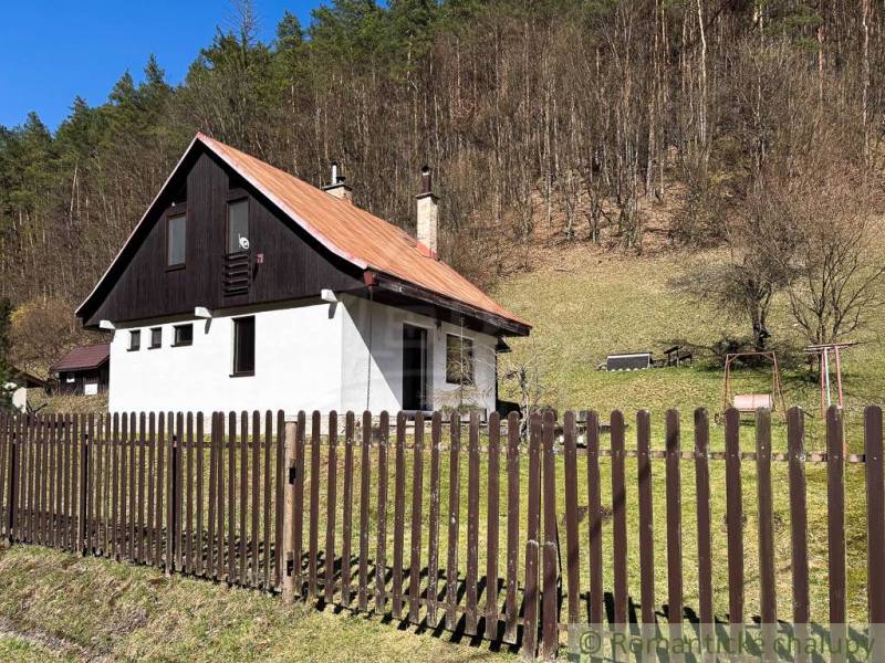 A cottage in Moštenica surrounded by a fence and forest, nestled in nature.