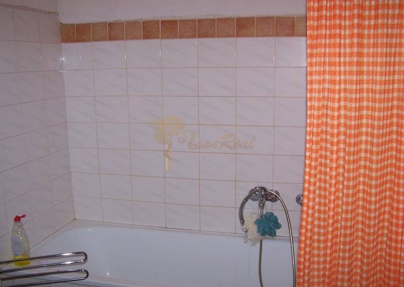 Bathroom with a bathtub, orange curtain, and tiles in a 2-room apartment.