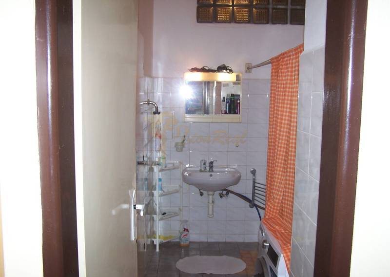 Bathroom in a 2-room apartment with a white sink, shower, and orange curtain.