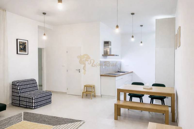Interior of a 2-room apartment with a simple white kitchen and wooden furniture.