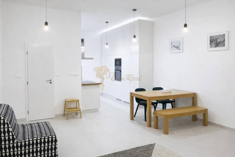 Interior of a 2-room apartment with white walls, a wooden table, and a black sofa.
