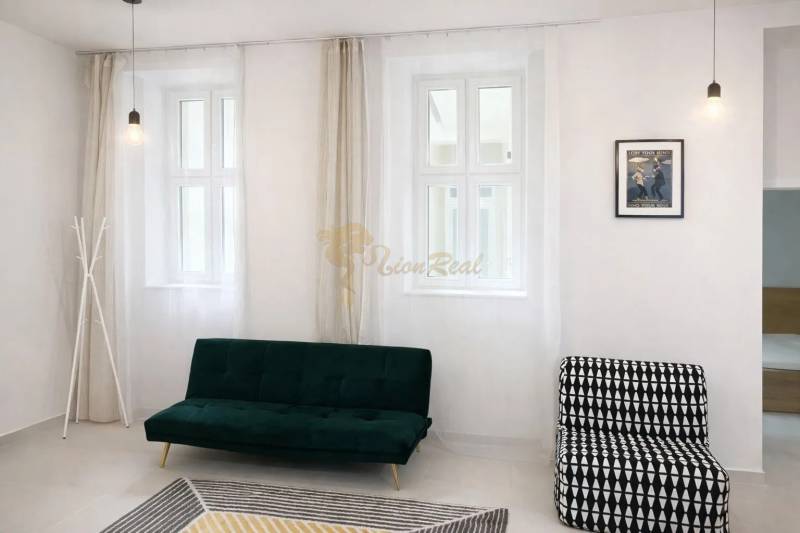 Living room with white walls, a green sofa, a patterned armchair, and curtains.