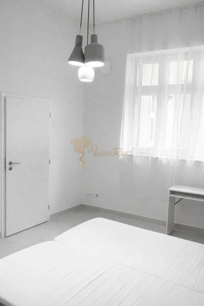 White room with a double bed, table, and pendant lighting in a 2-room apartment.