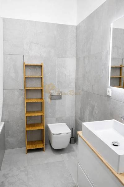 Bathroom in a 2-room apartment with gray tiles, a sink, and a shelf.