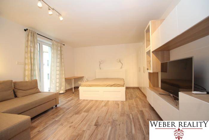 Living area in a studio apartment with a bed and a floor with a wood decor.