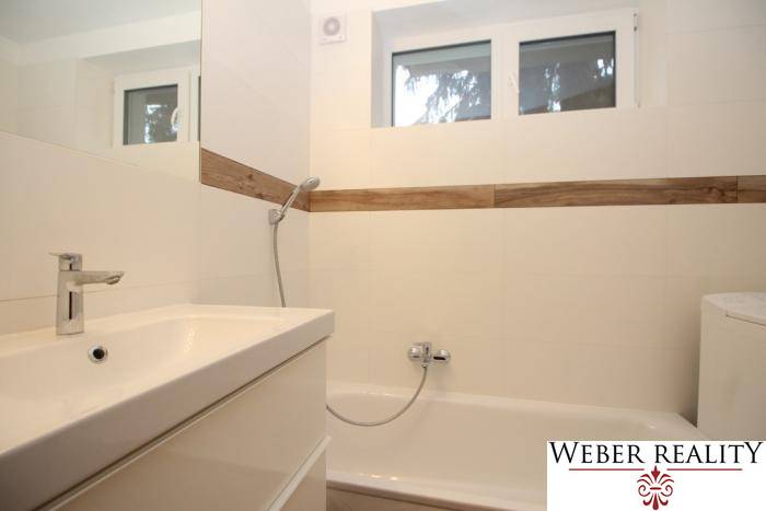 Bathroom with a bathtub and a sink in a studio apartment, white tiles, wooden decor.