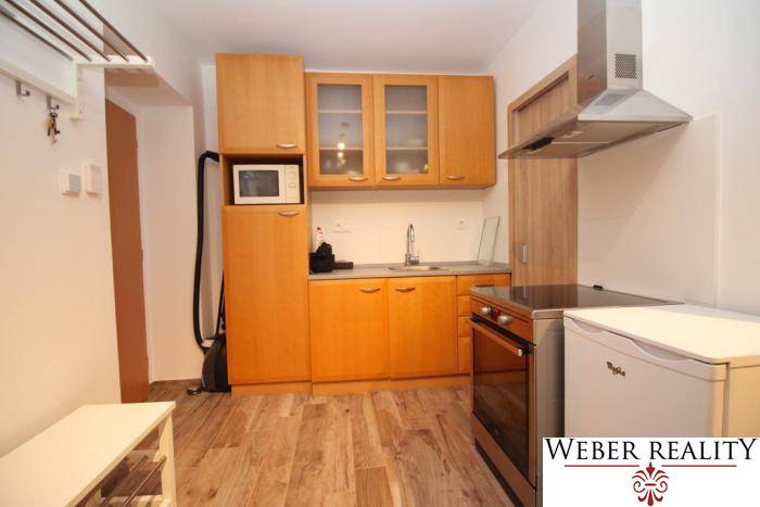 Kitchen in a studio apartment with a wood-patterned floor, light wooden cabinets.