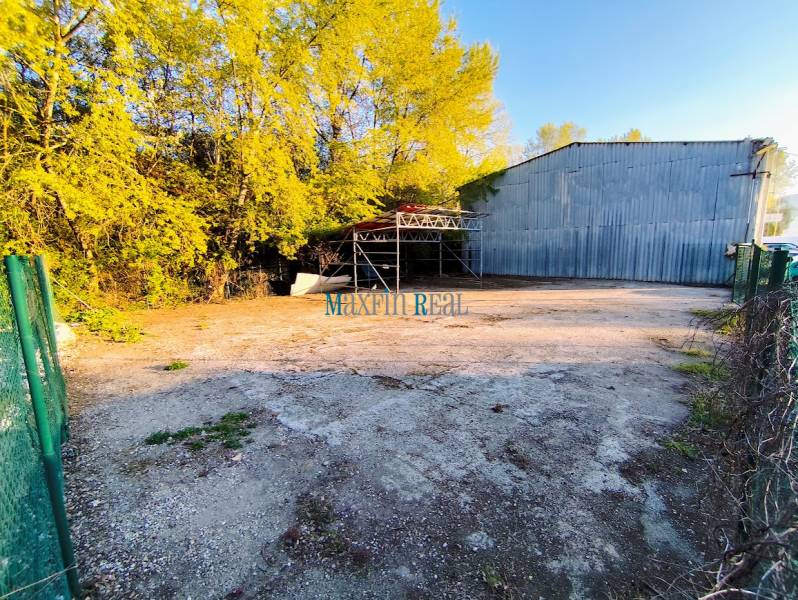 Commercial land in Nitra with a metal hall and fencing in a wooded environment.