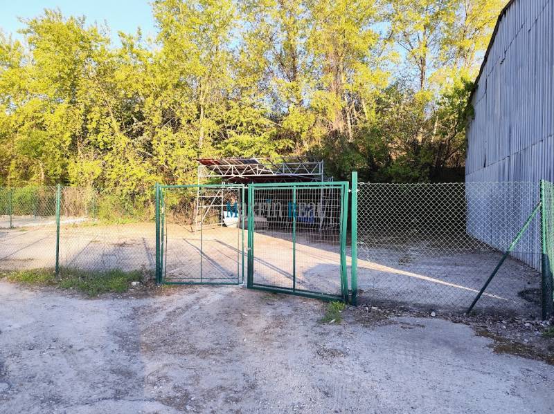 A fence with a gate and a metal structure surrounded by trees in the commercial area of Nitra.