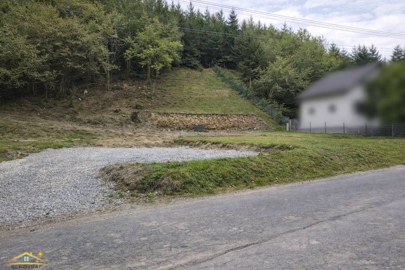 A sloped plot of land in the village of Makov with an access road and surrounding forest vegetation. Land - residential.