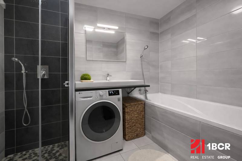 A bathroom in a 3-room apartment with a washing machine, shower, and bathtub, light tiles.