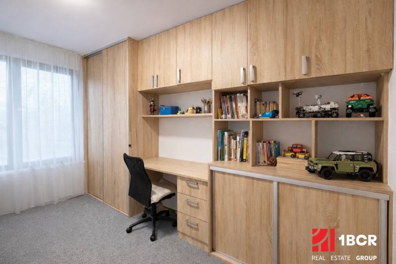 A workspace in a 3-room apartment with a wooden decor and plenty of shelves for books.