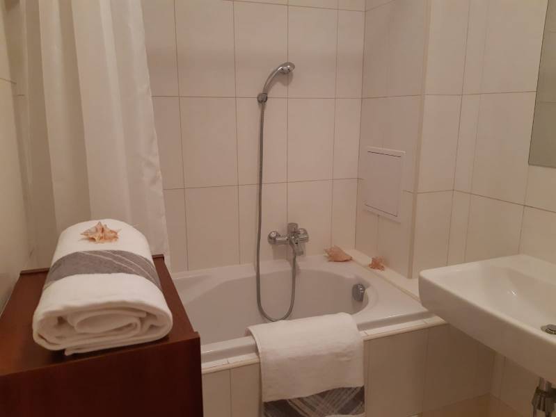 Bathroom with shower, bathtub, sink, and white towels, suitable for a 3-room apartment.