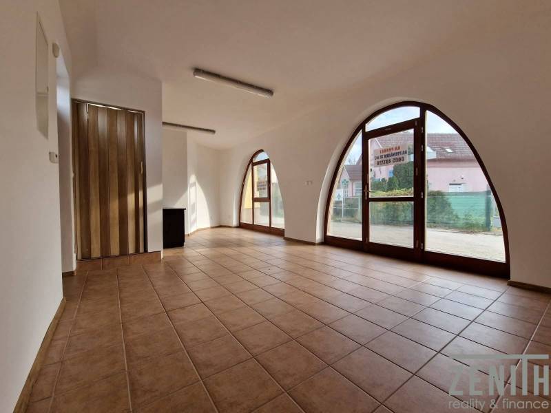 Interior of commercial spaces with large arched windows, tiled floor, and wooden doors.