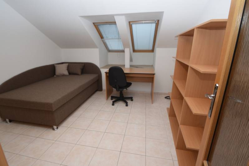 A room in a family house with a bed, table, shelves, tiles, and skylights.