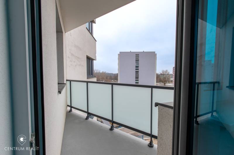 A balcony in a 2-room apartment with a view of the surrounding buildings through a glass railing.