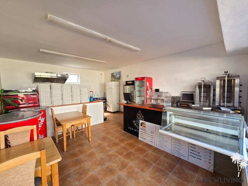 Interior of a gastro space with a counter, refrigerated display cases, and a stack of pizza boxes.