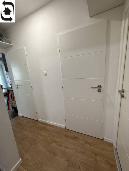 A hallway in a 4-room apartment with white doors and a wooden decor floor.