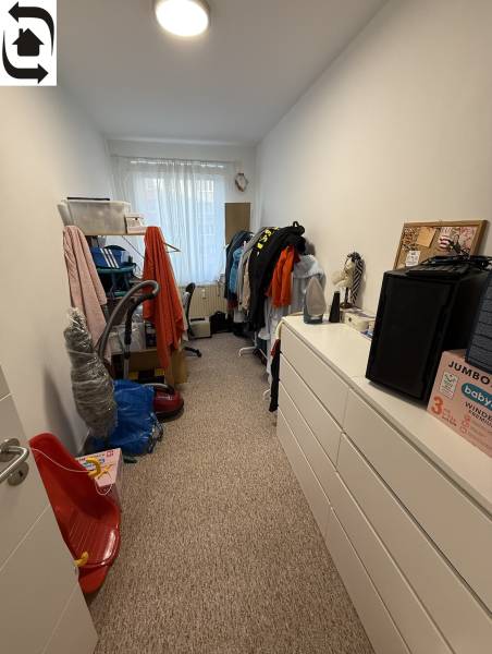 A room with wardrobes and clothes in a 4-room apartment, dominated by white walls and carpet.