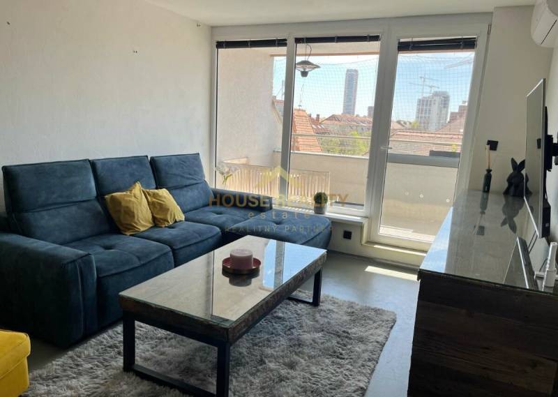 Living room in a 3-room apartment with a dark couch, a coffee table, and large windows.