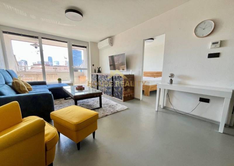 Living room of a three-room apartment with a sofa, television, and balcony.