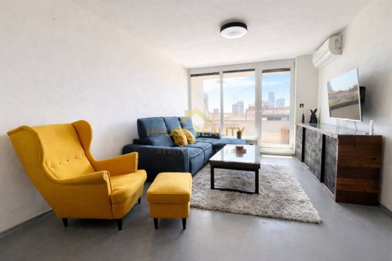 Living room in a 3-room apartment with a yellow armchair, a blue sofa, and a TV on the wall.