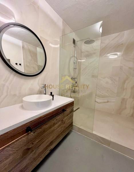 Bathroom with a wooden cabinet, round mirror, and shower in a 3-room apartment.