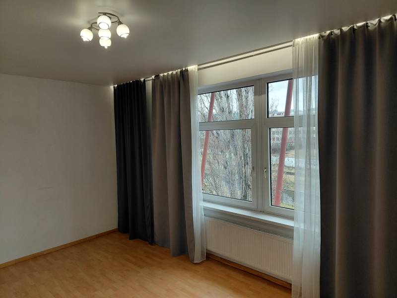 A room with a large window, blackout curtains, and a floor with a wooden decor. Commercial spaces.