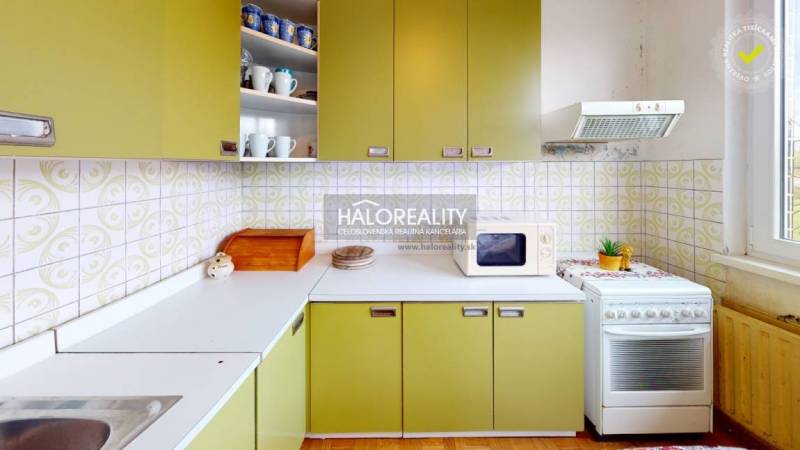 A kitchen in a family house with retro green cabinets and a microwave on a white countertop.