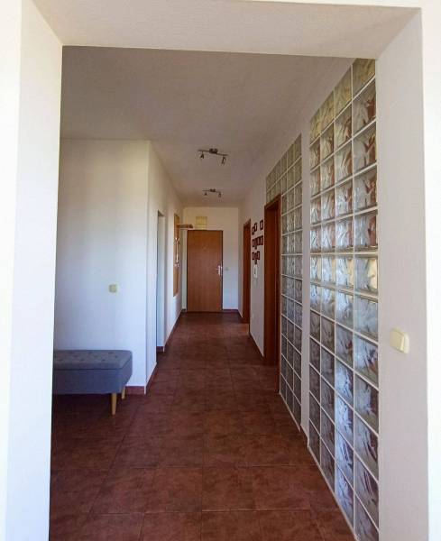 A hallway in a 3-room apartment with brown tiles and a glass block wall.