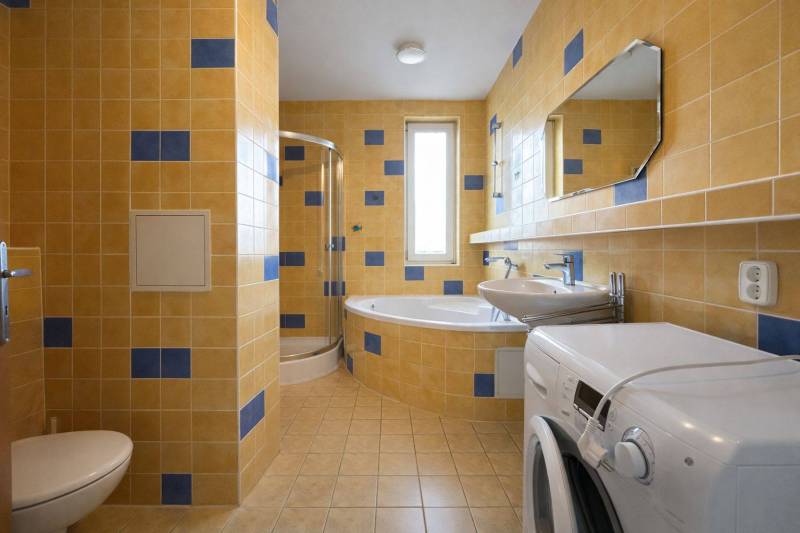 A bathroom in a 3-room apartment with a bathtub, shower, and washing machine, tiled with yellow tiles.