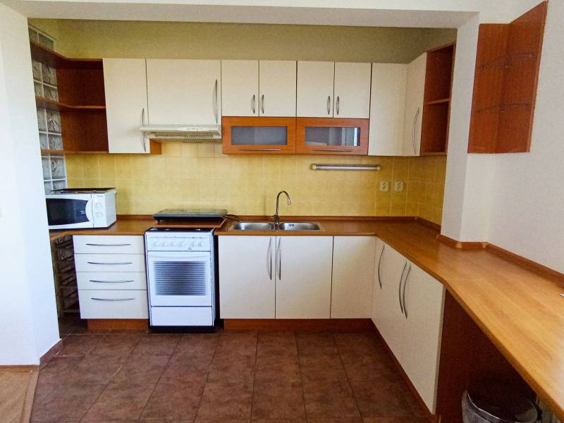 A kitchen in a 3-room apartment with a combination of white furniture and a wooden decor floor.
