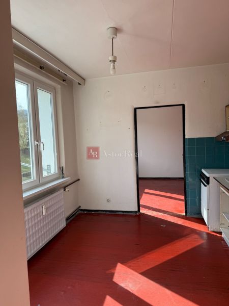 A kitchen of a 2-room apartment with a red floor and a window, light walls, dark tiles.