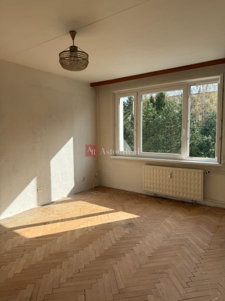 A room with a large window, a chandelier, and a floor with a wooden decor, a 2-room apartment.