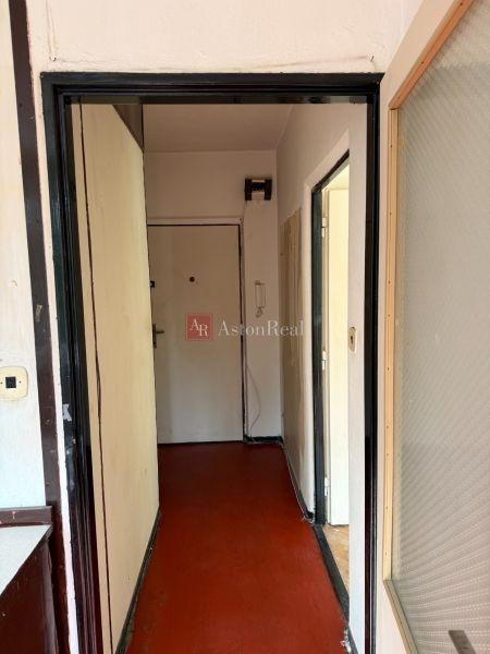 A hallway in a 2-room apartment with light paint and red linoleum flooring.