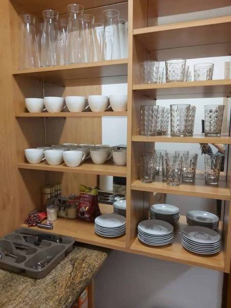 Kitchen cabinet with glasses, bowls, and cutlery on wooden shelves.