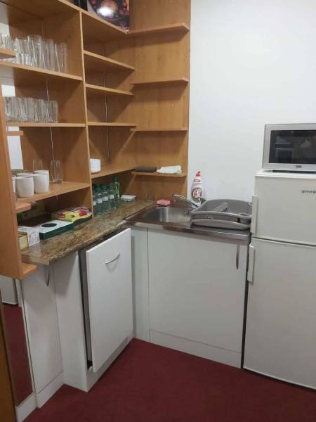 Kitchen corner in offices with appliances, wooden shelves, and red flooring.